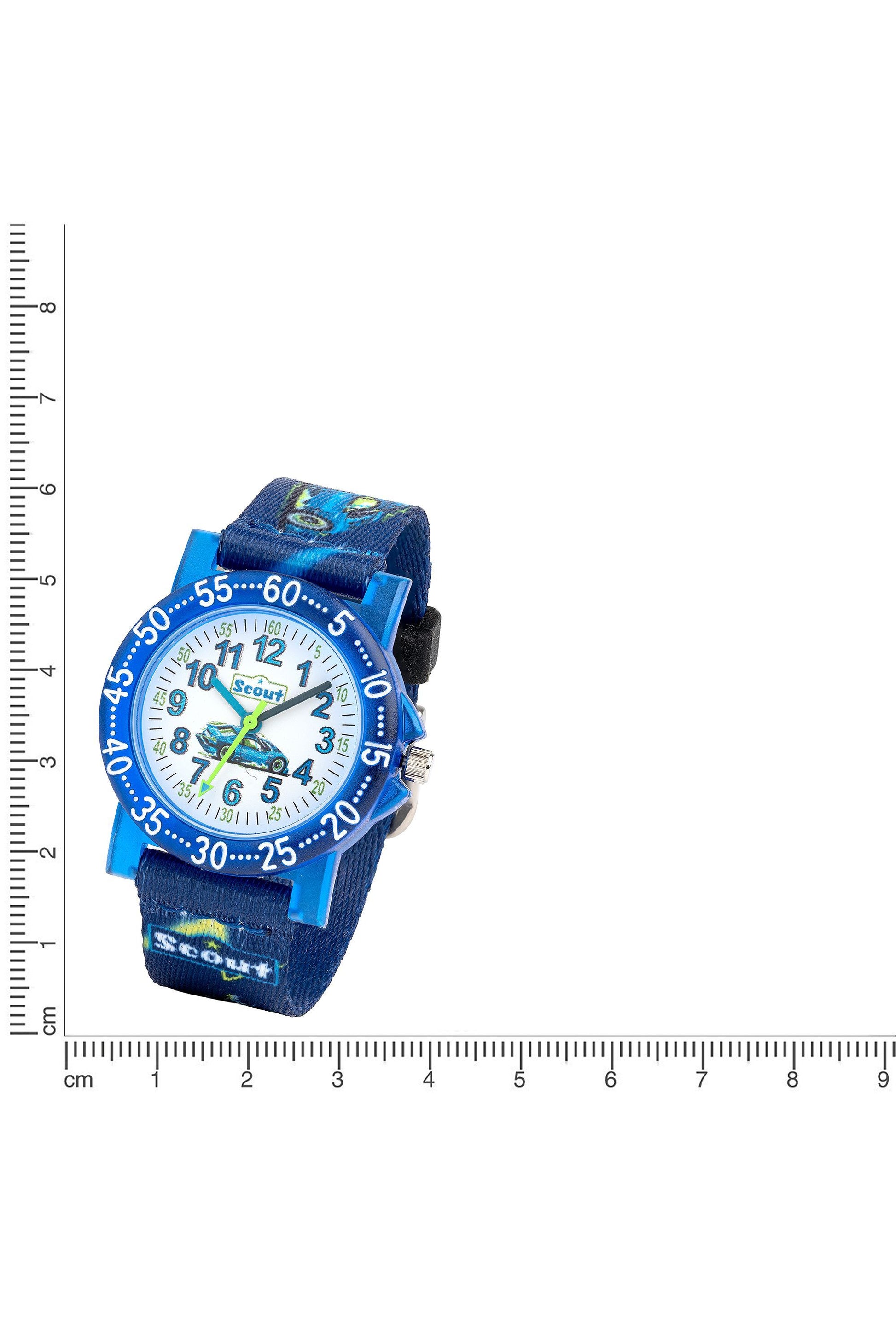 Scout Kinderuhr mit grün-blauem Textilband, Rennwagen-Motiven und weißem Lernzifferblatt neben einem Lineal zur Größendarstellung